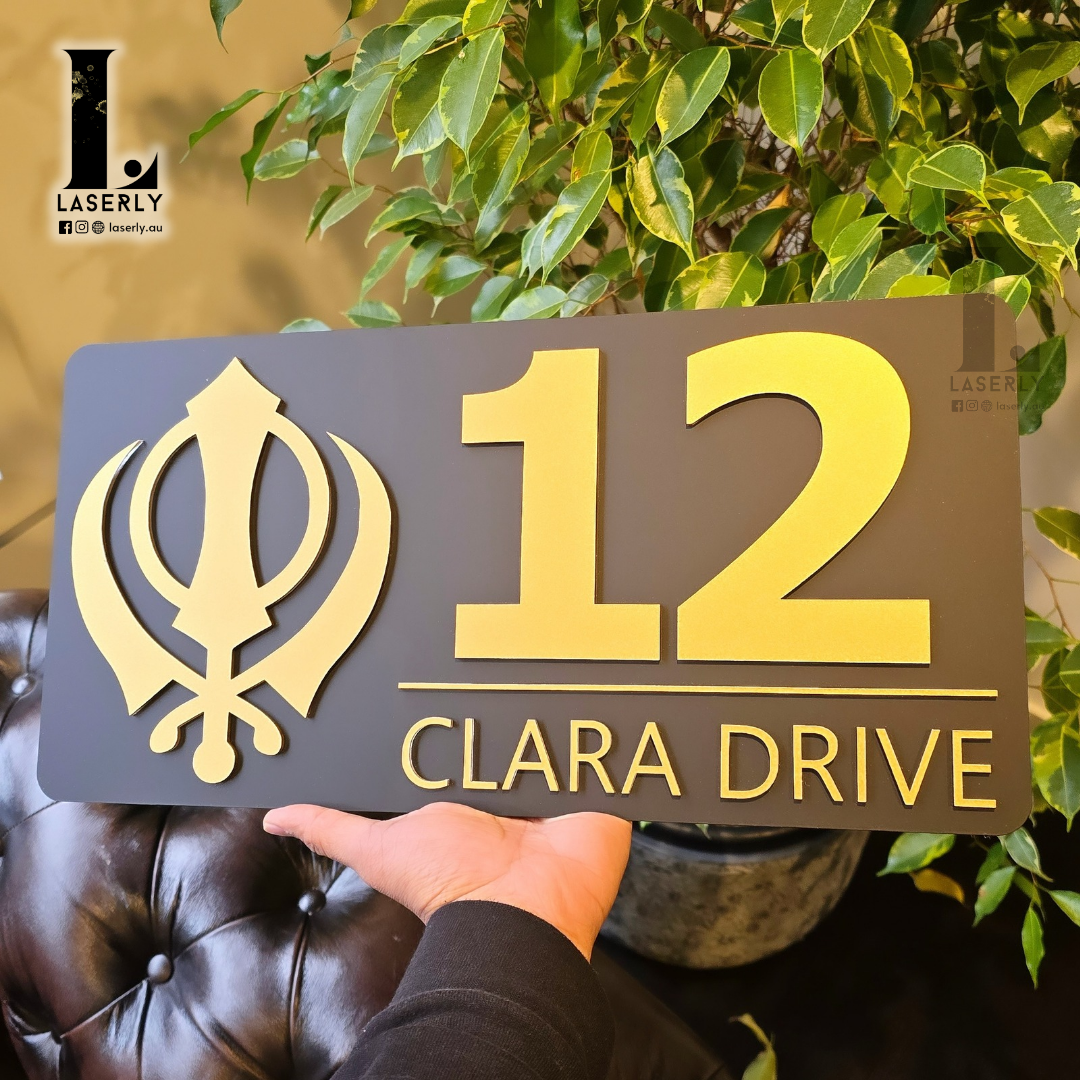 Modern Sikh Kandha house number sign in black and gold finish near doorway.