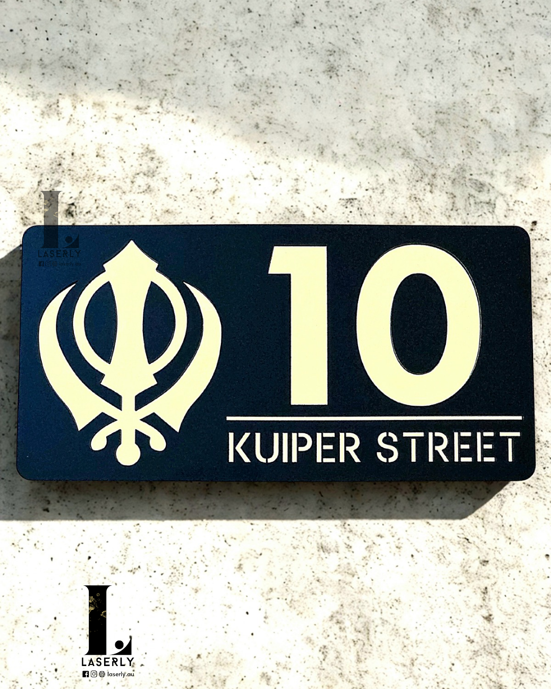 Kandha house number plaque in black acrylic with metallic gold lettering mounted on exterior wall.