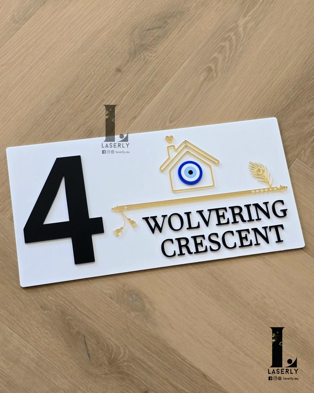 Modern white house number sign with evil eye accent beside home entrance.